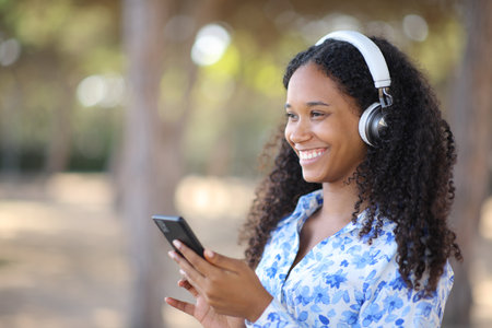 Happy black woman wearing headphone listening music holding phone outsideの写真素材