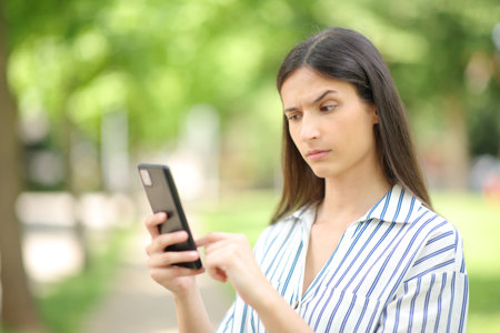 Suspicious woman checking strange news on phone in a parkの写真素材