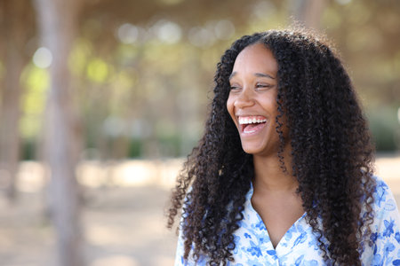 Joyful black woman laughing loud standing in a park looking at sideの写真素材