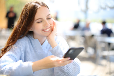Happy woman in a bar terrace watching phone content a sunny dayの写真素材