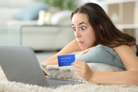 Perplexed online buyer paying with laptop and credit card on the floor at homeの写真素材
