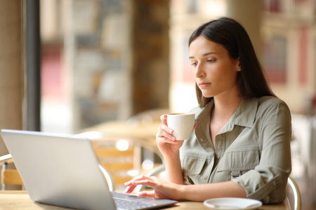 Woman using laptop drinking in a coffee shop terraceの写真素材