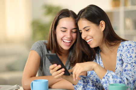 Happy women checking online content on phone and laughing at homeの写真素材