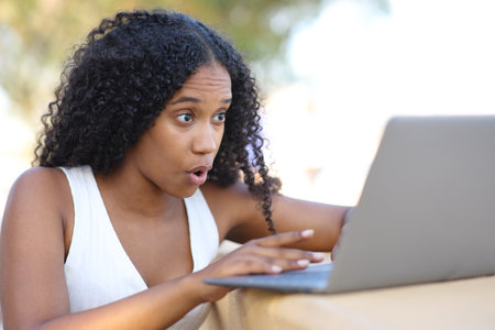 Amazed black woman checking laptop outdoorsの写真素材