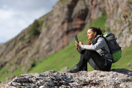 Hiker using phone sitting on a rock in the mountainの写真素材
