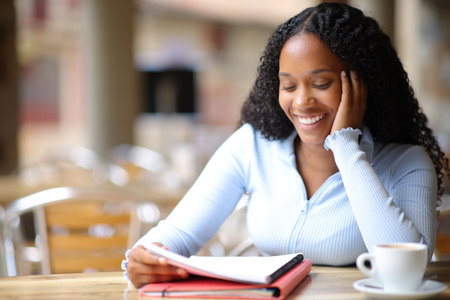 Happy black student memorizing notes in a coffee shop terraceの写真素材