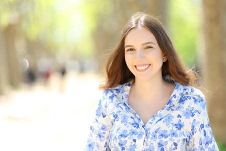Front view portrait of a happy woman smiling at camera standing in a park on a sunny dayの写真素材