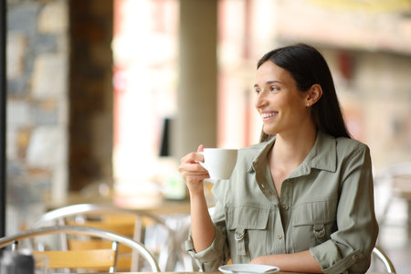 Happy woman sitting in a coffee shop drinking contemplatingの写真素材