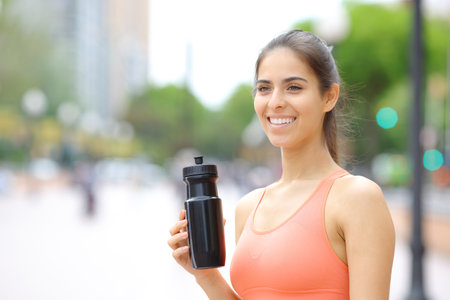 Happy runner holding water bottle after sport in the streetの写真素材