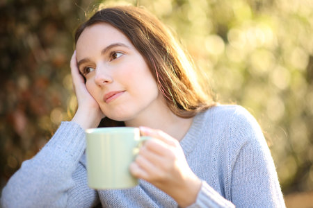 Woman dreaming looking away drinking coffee sitting in a gardenの写真素材