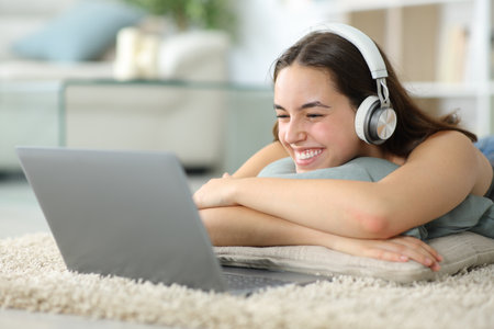 Happy woman watching media content on laptop lying on a carpet at homeの写真素材