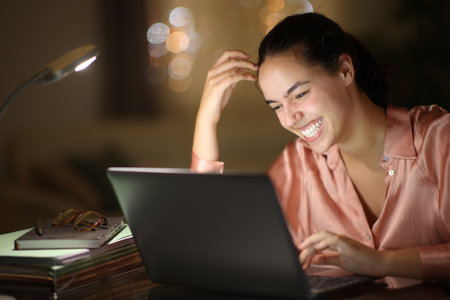 Tele worker in the night laughing checking laptop at homeの写真素材