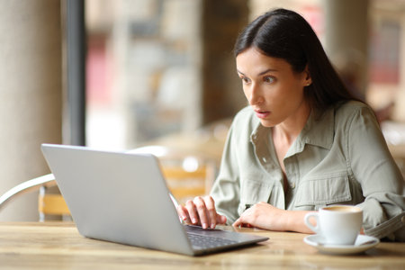Stunned woman checking news on laptop in a bar terraceの写真素材