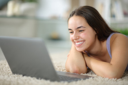 Happy woman lying on the floor watching media on laptop at homeの写真素材