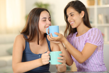 Two friends drinking coffee and smelling at homeの写真素材