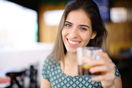 Portrait of a happy woman offering soda to you in a restaurantの写真素材