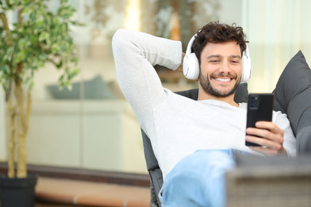 Happy man in a terrace watching media on phone lying on a couchの写真素材