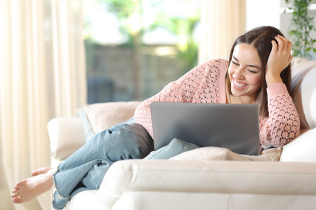 Happy woman using laptop sitting on a sofa at homeの写真素材