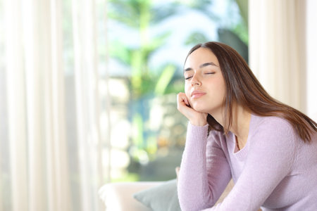 Woman relaxing sitting on a sofa with closed eyes at home with a garden on backgroundの写真素材