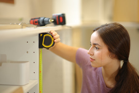 Woman taking measure of a kitchen furniture with a measure tape in a house under renovationの写真素材