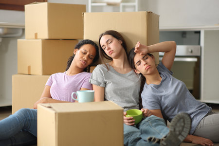 Three tired multi ethnic women moving house resting sitting on the floorの写真素材