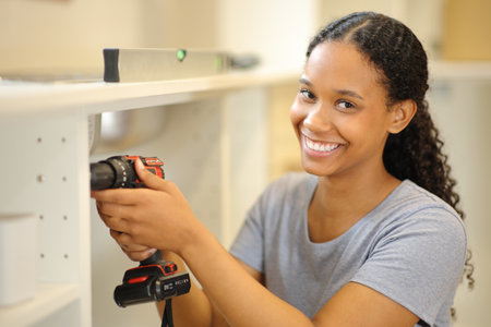 Black woman assembling furniture looking at you in a house under renovationの写真素材