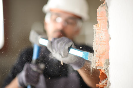 Construction worker using escarpment and hammer to wrek a wall in a house