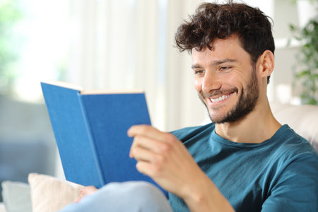 Happy man reading a paper book sitting on a couch at homeの写真素材