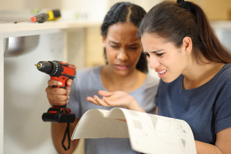 Two confused women reforming house reading furniture instruction manual in the kitchenの写真素材