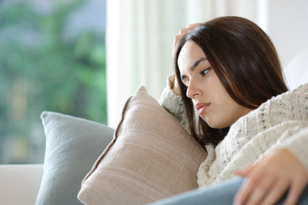 Worried woman lying on a couch looking away at homeの写真素材