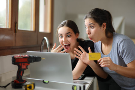 Two excited women renovating house buying online with laptop and credit card in the kitchenの写真素材