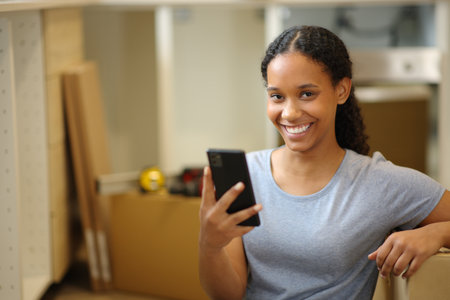 Happy black woman holding phone moving house looking at you