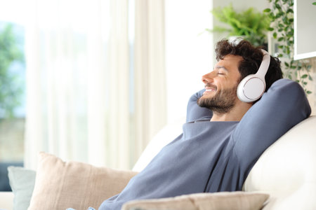 Profile of a happy man listening music with headphone and relaxing on a couch at homeの写真素材