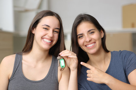 Front view portrait of two happy roommates showing keys moving houseの写真素材