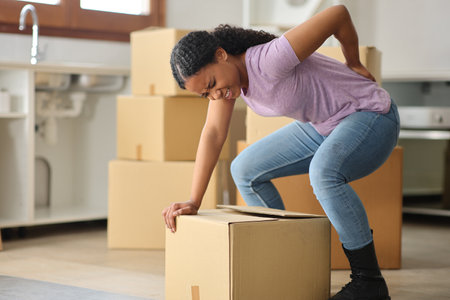 Black tenant moving house suffering backache lifting box in the kitchenの写真素材