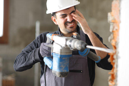 Construction worker suffering accident in an eye working with a rotary hammer without protection glassesの写真素材