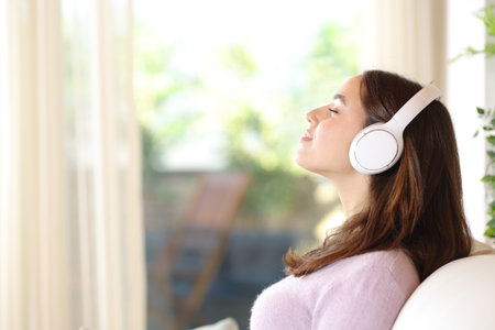 Profile of a woman relaxing listening chill music sitting on a sofa at homeの写真素材