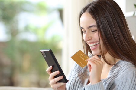 Happy woman buying online with credit card and phone in a house interiorの写真素材