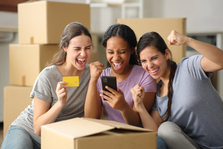 Three excited multi ethnic roommates buying online with credit card and laptop moving houseの写真素材