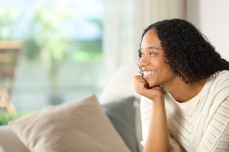 Happy black woman contemplating the garden through a window in a luxury houseの写真素材