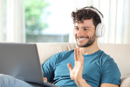 Happy man having video call on laptop sitting on a couch at homeの写真素材