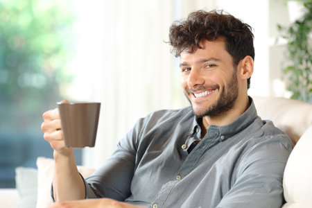 Happy man holding coffee cup looking at camera in a houseの写真素材