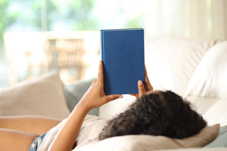 Black woman watching blank book cover lying on a couch at homeの写真素材