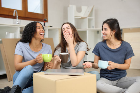 Funny roommates laughing resting and drinking while moving houseの写真素材