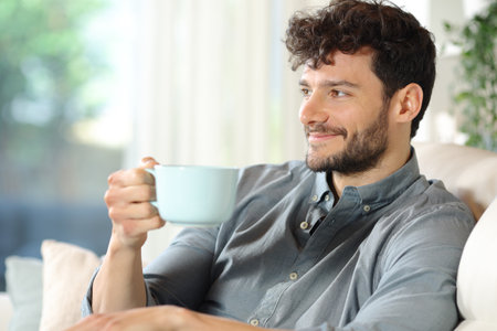 Happy man drinking coffee sitting in a house interior looking awayの写真素材