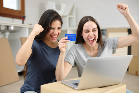 Two excited roommates moving house buying online and finding offer on laptopの写真素材