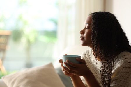 Side view portrait of a black woman at home drinking coffee and relaxing with eyes closedの写真素材