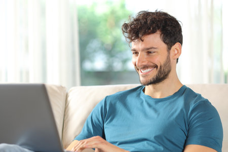 Happy man is using laptop sitting on a couch at homeの写真素材