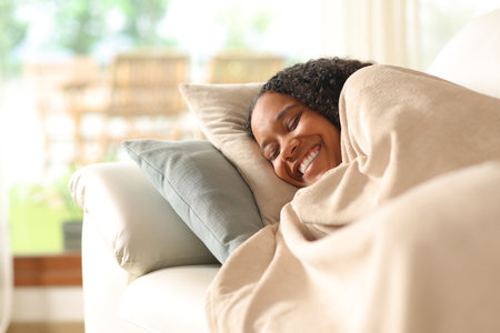 Happy black woman napping lying on a couch at homeの写真素材