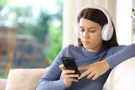 Woman listening online audio with headphone and smart phone sitting on a couch at homeの写真素材